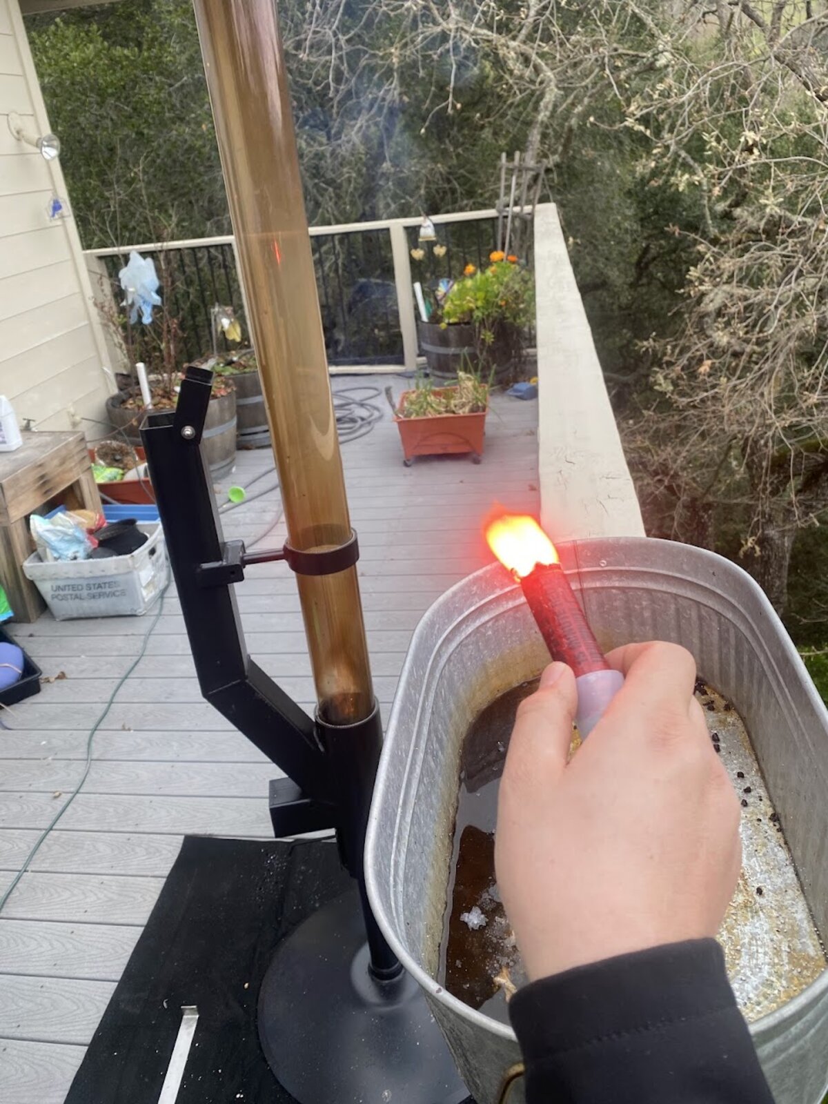 The FlameCam detection sensor on a stand on a deck, aimed across the yard at a hand-held road flare burning in a galvanised tub of water.